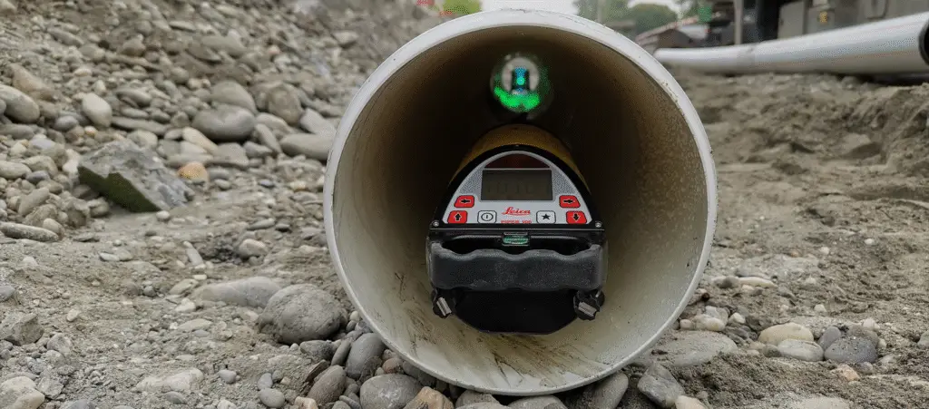 Pipe with construction laser inside on gravel.