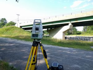 A Leica MS60 Nova MultiStation is standing next to a bridge.