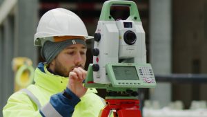 A man in a hard hat is holding a Leica MS60 Nova MultiStation.