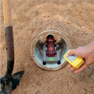 A person is holding a Leica Piper 100/200 Piper Laser Packages - Red Beam in a hole in the sand.