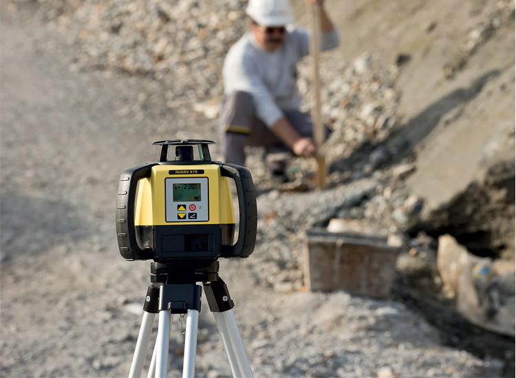 Yellow laser level on tripod at construction site.