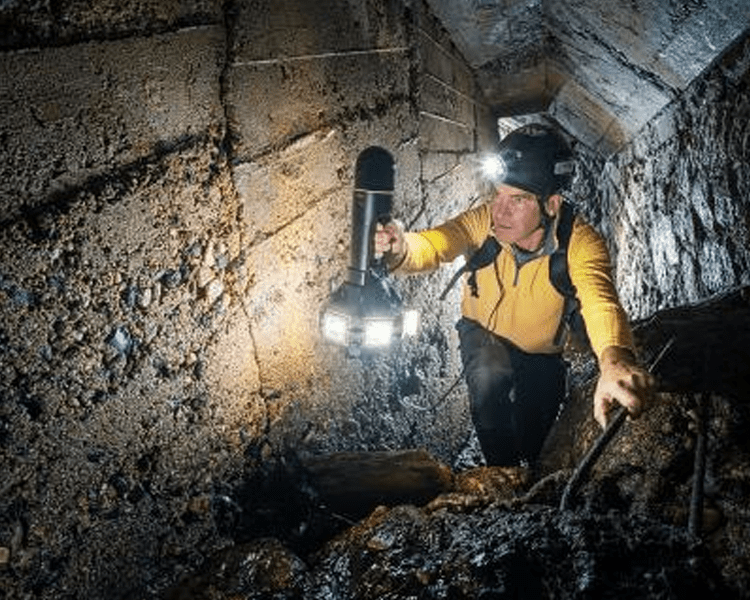 Person exploring a tunnel with a flashlight.