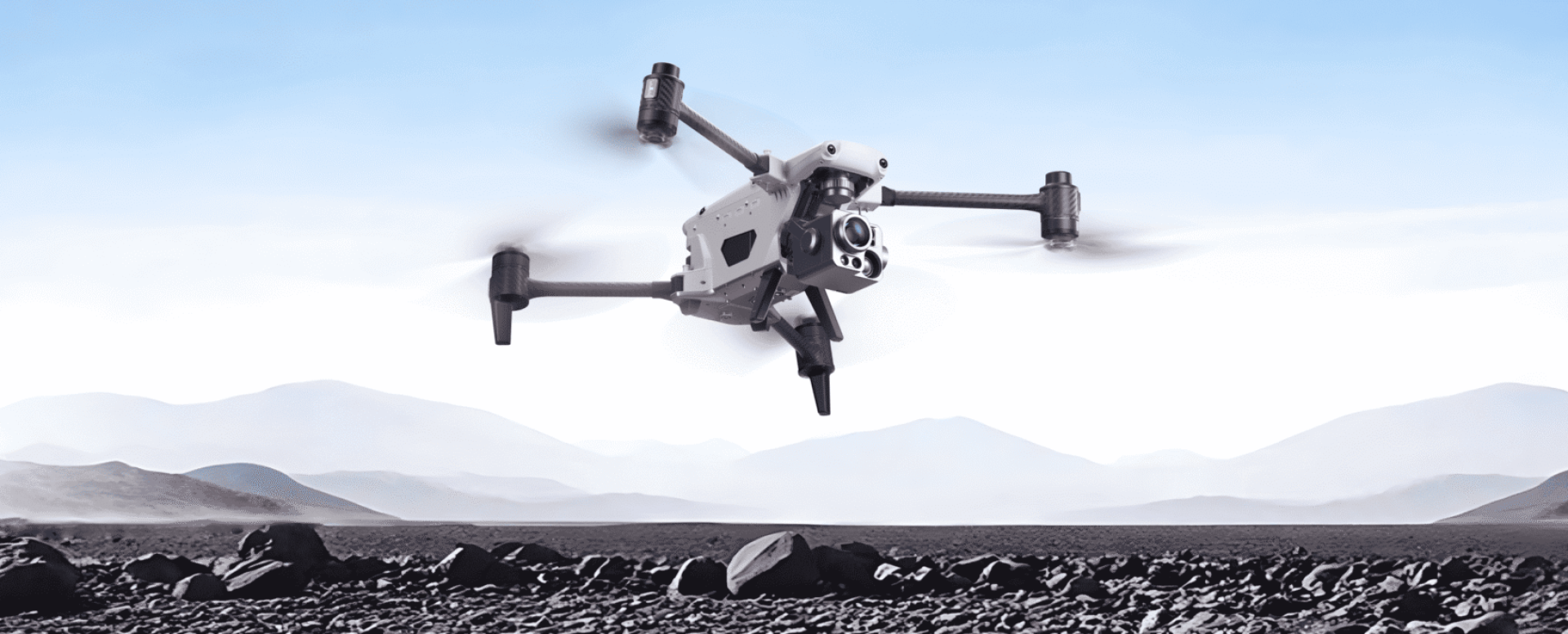 Drone flying over rocky landscape, mountains behind.